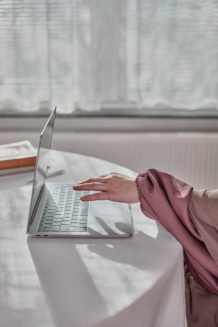 A hand in an elegant sleeve uses a laptop indoors with soft natural light.